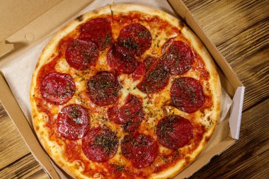 Tahta bir masanın üzerindeki karton kutuda nefis taze pizza. Üst Manzara. Yemek teslimatı, fast food, pizza teslimatı.