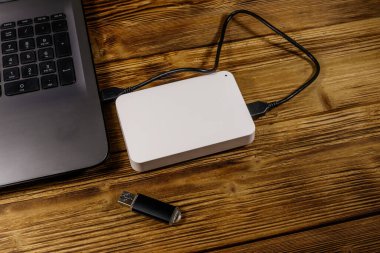 Harici HDD, tahta bir masadaki dizüstü bilgisayara ve USB flash diske bağlı. Veri depolama kavramı