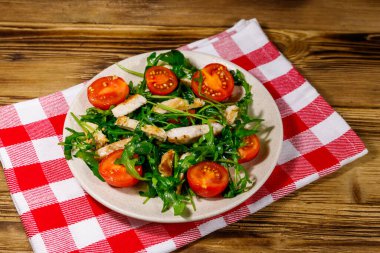 Lezzetli tavuk göğsü salatası, taze roka ve ahşap masada kiraz domatesleri.