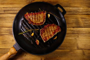 Biberiyeli ızgara domuz bifteği, sarımsak ve ahşap masada ızgara demir tavada baharat. Üst görünüm