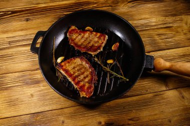 Biberiyeli ızgara domuz bifteği, sarımsak ve ahşap masada ızgara demir tavada baharat. Üst görünüm
