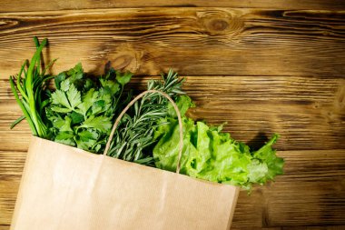 Yeşil soğanlı kağıt torbası, biberiye, marul yaprakları ve ahşap masada maydanoz. Üst Manzara. Sağlıklı gıda ve market alışverişi kavramı