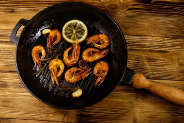 Baharatlı ızgara karides, biberiye ve limon ahşap bir masada ızgara kızartma tavasında. Üst görünüm