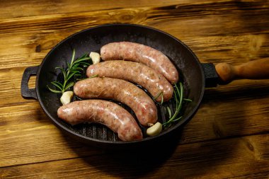 Çiğ sosisler hazır biberiye, sarımsak ve baharatlarla ahşap masada ızgara ızgara demir tavada.