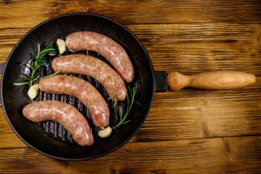 Çiğ sosisler hazır biberiye, sarımsak ve baharatlarla ahşap masada ızgara ızgara demir tavada. Üst görünüm
