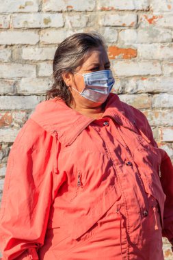 Kıdemli kadın yüzünde Coronavirus ve diğer virüs ve hastalıklara karşı koruyan tıbbi bir maske takıyor. Eski tuğla duvarın arka planında. Koronavirüs salgını