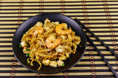 Tayland usulü kızarmış pirinç eriştesi, karides ve bambu hasırında soya peyniri. Tayland yemeği.