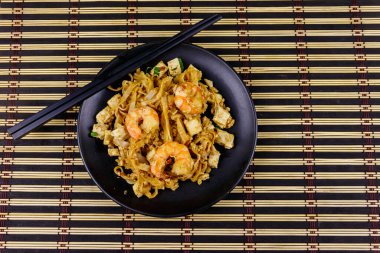 Tayland usulü kızarmış pirinç eriştesi, karides ve bambu hasırında soya peyniri. Üst Manzara. Tayland yemeği.