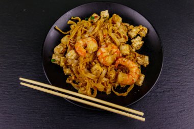 Kızarmış pirinç eriştesi, karidesli Pad Thai ve siyah arkaplanlı bir tabakta tofu. Üst Manzara. Tayland yemeği.
