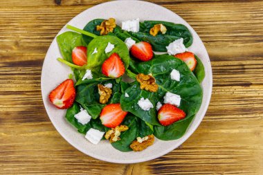 Çilekli, ıspanaklı, cevizli ve ahşap masadaki peynirli taze sağlıklı salata. Üst görünüm