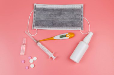 Koronavirüsü önleme ve tedavi etme kavramı. Tıbbi maske, el dezenfektanı, elektronik termometre, haplar, şırınga, pembe arka planda ampuller. Üst görünüm