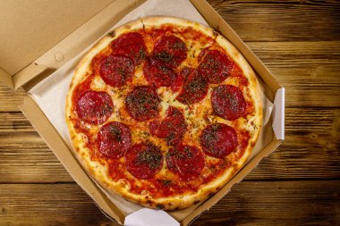 Tahta bir masanın üzerindeki karton kutuda nefis taze pizza. Üst Manzara. Yemek teslimatı, fast food, pizza teslimatı.