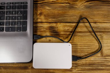 Harici HDD, tahta bir masadaki dizüstü bilgisayara bağlı. Üst Manzara. Veri depolama kavramı