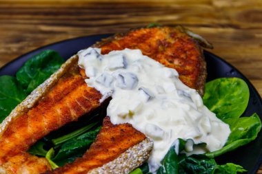 Ahşap masada ıspanaklı ve tartar soslu ızgara somon bifteği.