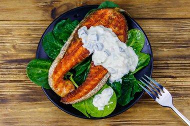 Ahşap masada ıspanaklı ve tartar soslu ızgara somon bifteği. Üst görünüm