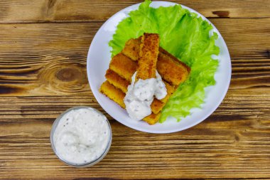 Tabakta kızarmış balık kroket, marul ve ahşap masada tartar sosu. Üst görünüm