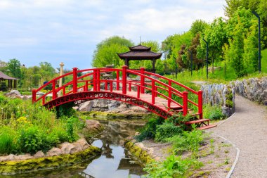 Japon bahçesindeki bir göletin yanında kırmızı köprü ve çardak.
