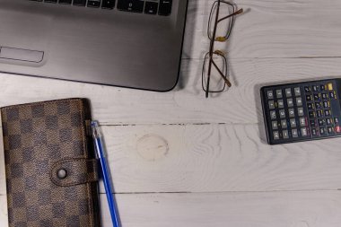 Bilgisayarı, hesap makinesi, not defteri, gözlüğü ve kalemi olan beyaz ofis masası. Üst görünüm, alanı kopyala