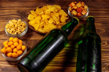Bira şişeleri ve ahşap masada bira için çeşitli atıştırmalıklar.