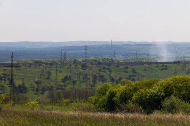 Enerji hatları, yeşil tepeler ve ağaçlarla dolu yaz manzarası