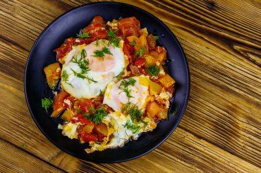 Ev yapımı shakshuka - kızarmış yumurta, soğan, dolmalık biber, domates ve dereotlu ahşap masa. Yahudi mutfağı. Üst görünüm