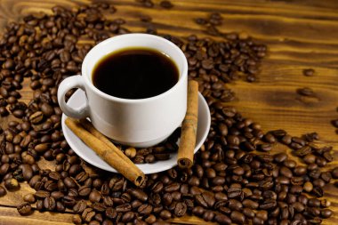 Bir fincan kahve, kavrulmuş kahve çekirdekleri ve ahşap masada tarçın çubukları.