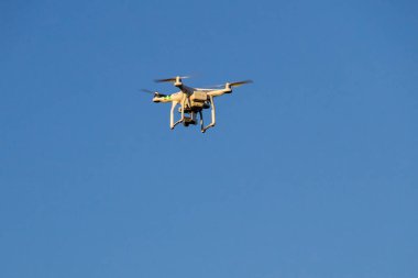 Mavi gökyüzünde süzülen kameralı bir kuadkopter.