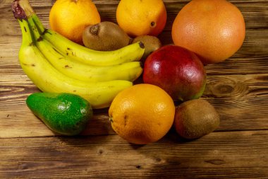 Ahşap masa üzerinde tropikal meyve çeşitleri. Muz, mango, portakal, avokado, greyfurt ve kivi ile natürmort