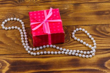 Ahşap arka planda hediye kutusu ve inci kolye.