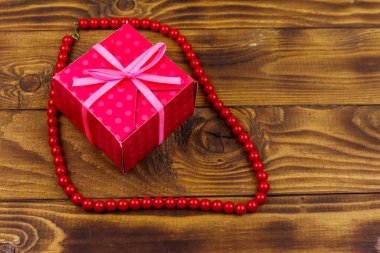 Ahşap arka plan üzerinde hediye kutusu ve kırmızı boncuk kolye