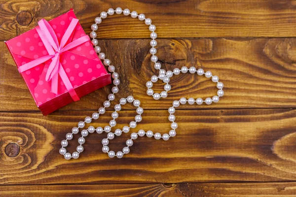 Ahşap arka planda hediye kutusu ve inci kolye.