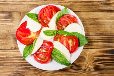 Domatesli İtalyan caprese salatası, ahşap bir masada mozzarella peyniri ve fesleğen. Üst görünüm