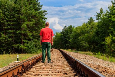 Yalnız adam tren yolunda yürüyor.