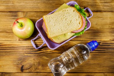 Sandviçli beslenme çantası, ahşap bir masada bir şişe su ve elma. Üst görünüm