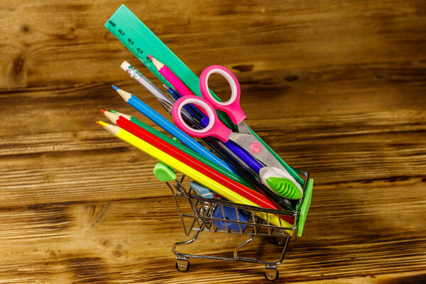 Buying school supplies. Shopping cart with school supplies on a wooden background. Back to school concept