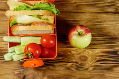 Elma ve beslenme çantası, sandviç ve taze sebzelerle ahşap bir masada. Üst görünüm