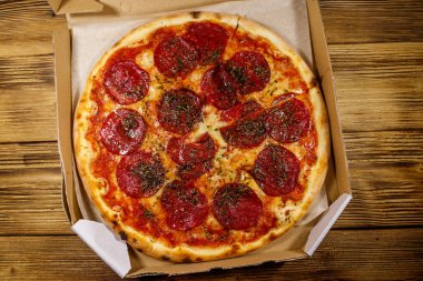 Tahta bir masanın üzerindeki karton kutuda nefis taze pizza. Üst Manzara. Yemek teslimatı, fast food, pizza teslimatı.