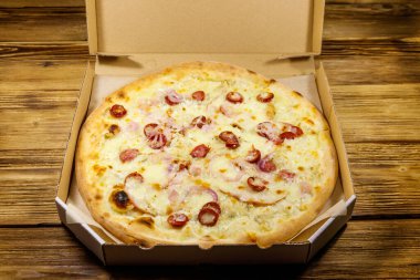 Tahta bir masanın üzerindeki karton kutuda nefis taze pizza. Yemek teslimatı, fast food, pizza teslimatı.