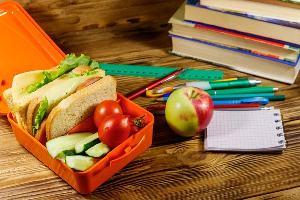 Okul konseptine geri dönelim. Okul malzemeleri, kitaplar, elma ve beslenme çantası içinde sandviçler ve ahşap bir masada taze sebzeler.