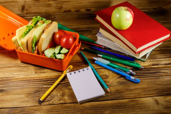 Okul konseptine geri dönelim. Okul malzemeleri, kitaplar, elma ve beslenme çantası içinde sandviçler ve ahşap bir masada taze sebzeler.