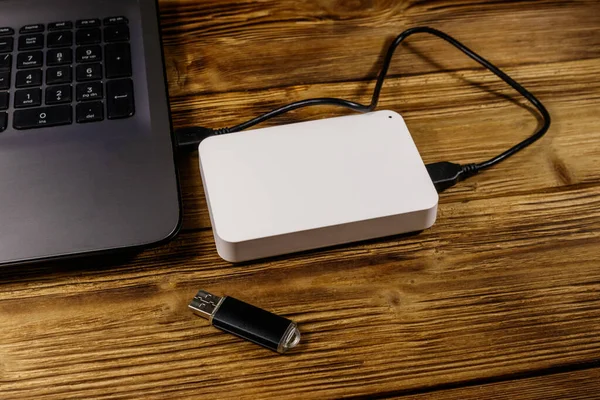 External HDD connected to laptop computer and USB flash drive on a wooden desk. Concept of data storage