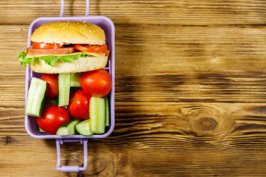 Hamburgerli beslenme çantası ve ahşap bir masada taze sebzeler. Üst görünüm, alanı kopyala