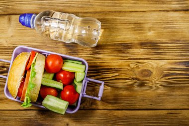 Bir şişe su ve hamburgerli beslenme çantası ve ahşap bir masada taze sebzeler. Üst görünüm, alanı kopyala