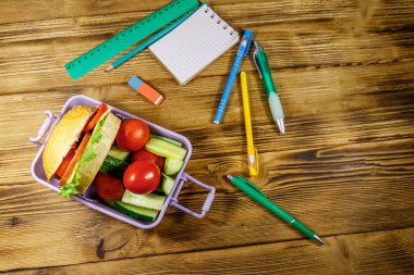 Okul konseptine geri dönelim. Okul malzemeleri, hamburgerler ve ahşap bir masada taze sebzeler.