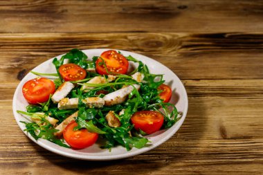 Lezzetli tavuk göğsü salatası, taze roka ve ahşap masada kiraz domatesleri.