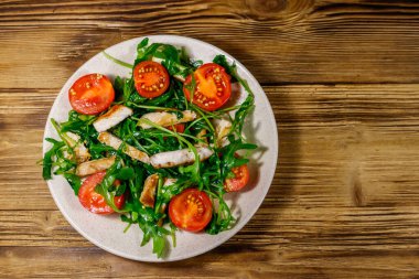 Lezzetli kızarmış tavuk göğsü salatası, taze roka ve ahşap masada kiraz domatesleri. Üst görünüm