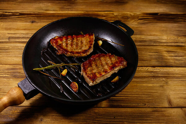 Grilled pork steaks with rosemary, garlic and spices in cast iron grill frying pan on wooden table