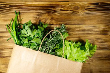 Yeşil soğanlı kağıt torbası, biberiye, marul yaprakları ve ahşap masada maydanoz. Üst Manzara. Sağlıklı gıda ve market alışverişi kavramı