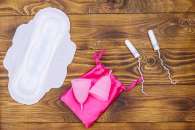 Adet pedi, tampon ve ahşap arka planda regl bardakları. Üst Manzara. Kritik günler, regl dönemi, kadın hijyeni
