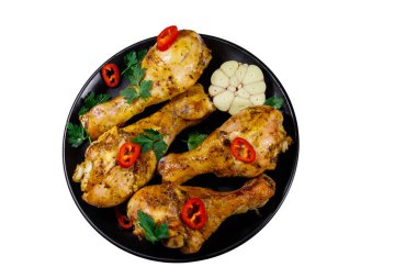 Beyaz arka planda izole edilmiş siyah bir tabakta baharatlı kızarmış tavuk budu. Üst görünüm